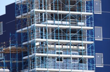 Paesaggio urbano con un edificio blu in costruzione, coperto da ponteggi.