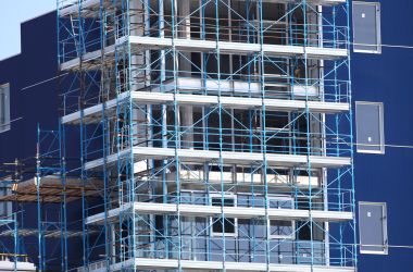 Paesaggio urbano con un edificio blu in costruzione, coperto da ponteggi.